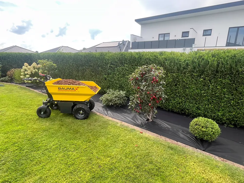 Elektro-Dumper mit Rindenmulch neben einer frisch geschnittenen Hecke