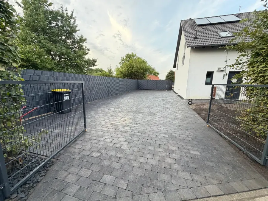 Dieselbe Zufahrt nachher: durchgehend gepflasterter Hof mit Sichtschutzzaun und Einfahrtstor