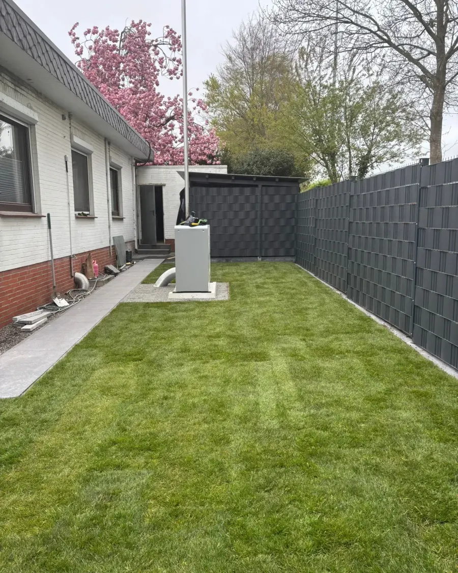 Derselbe Seitengarten nachher: dichter Rollrasen, neuer Plattenweg und anthrazitfarbener Sichtschutzzaun