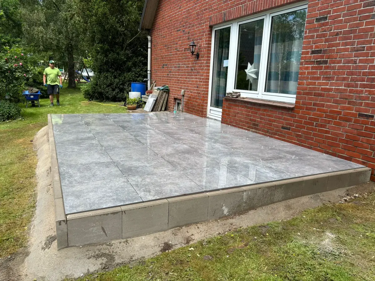 Dieselbe Terrasse nachher: großformatige graue Platten sauber verlegt bis an die Hauswand